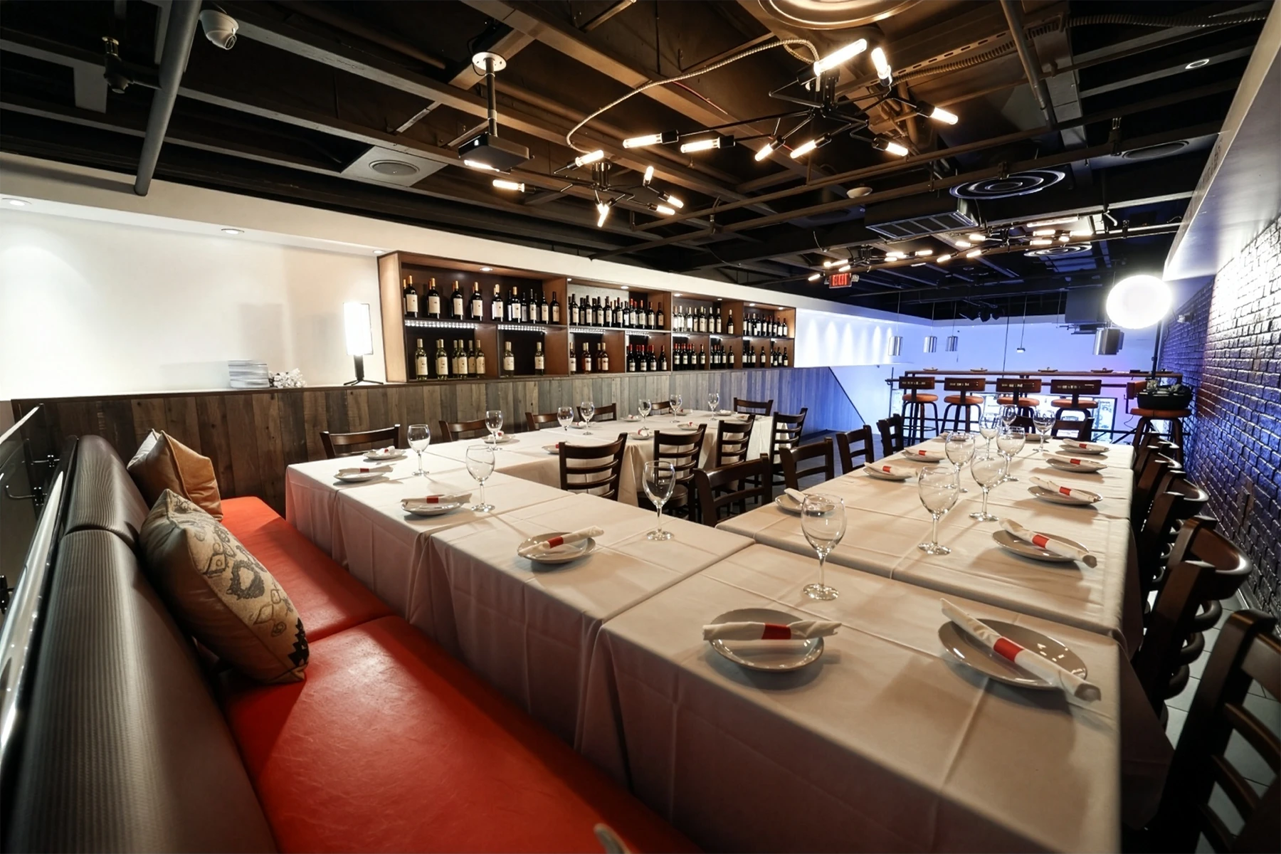The banquet room set with long linen tables, wine wall and red banquette seating