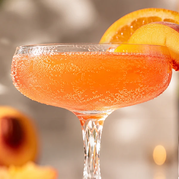 A coupe of sparkling peach mimosa garnished with orange and peach slices