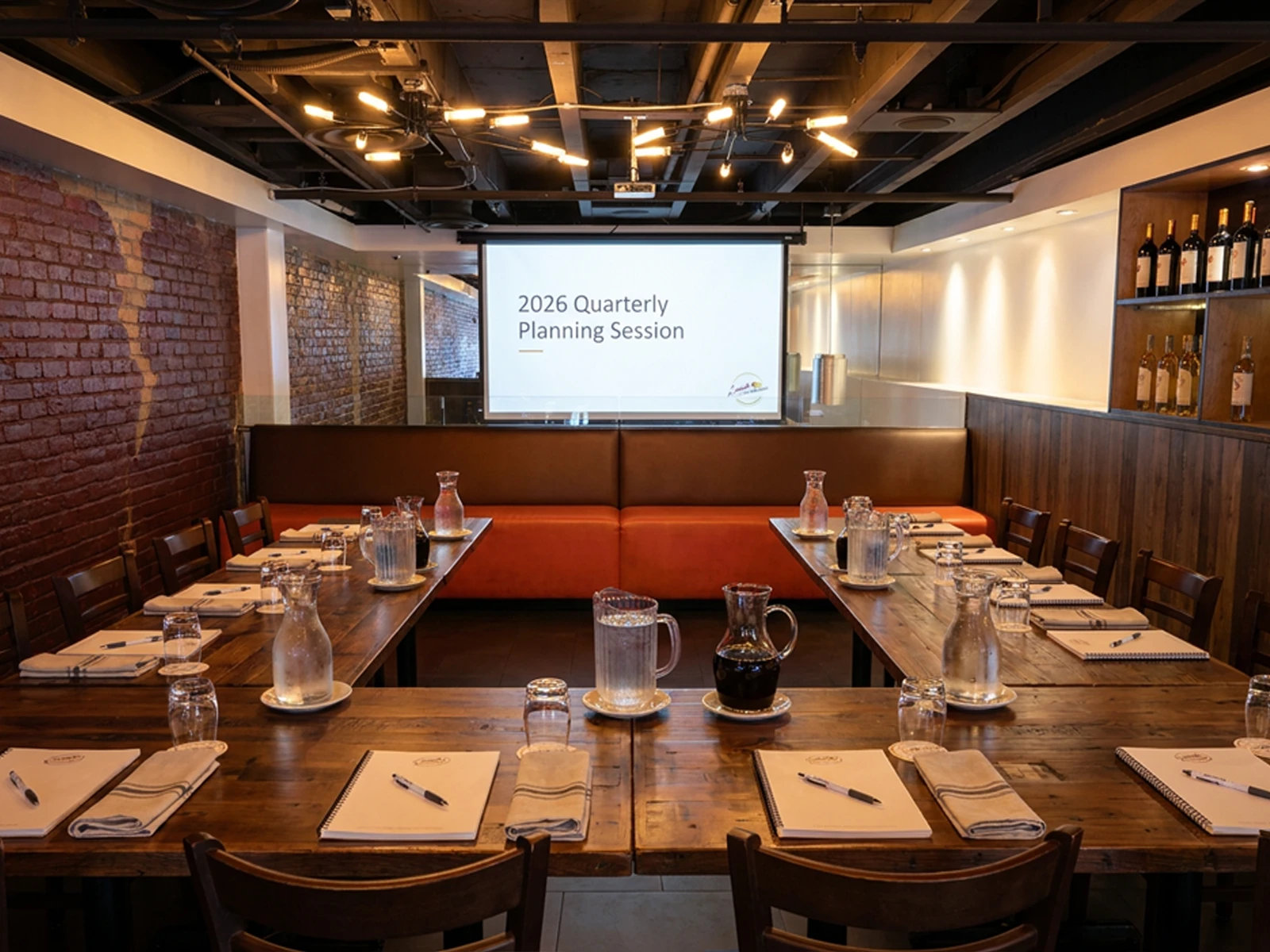 The banquet room set U-shape for a corporate meeting with notepads, water carafes and the projector screen lit