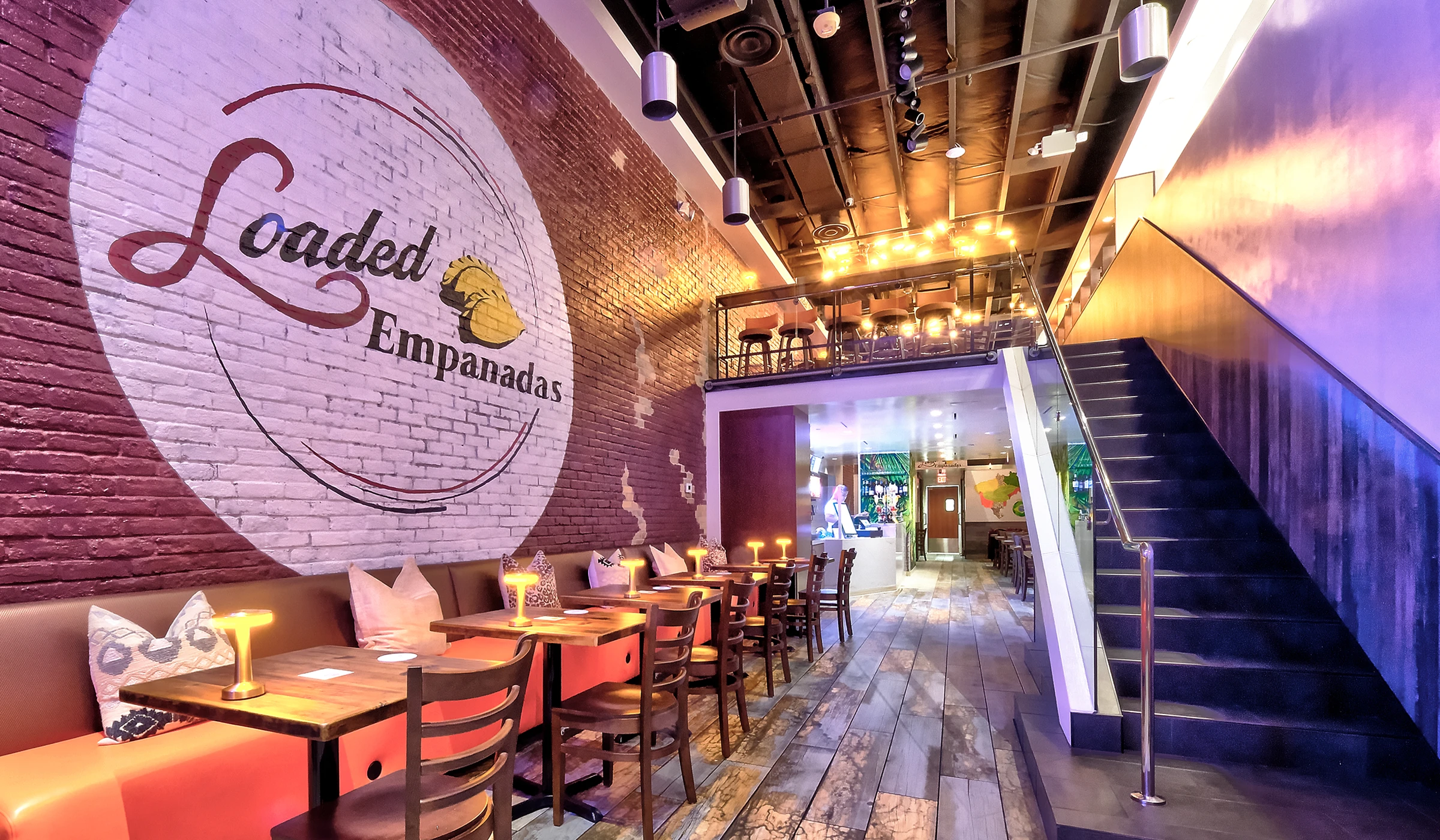 The Loaded Empanadas dining room with the painted logo mural on exposed brick, banquette seating and the mezzanine bar above