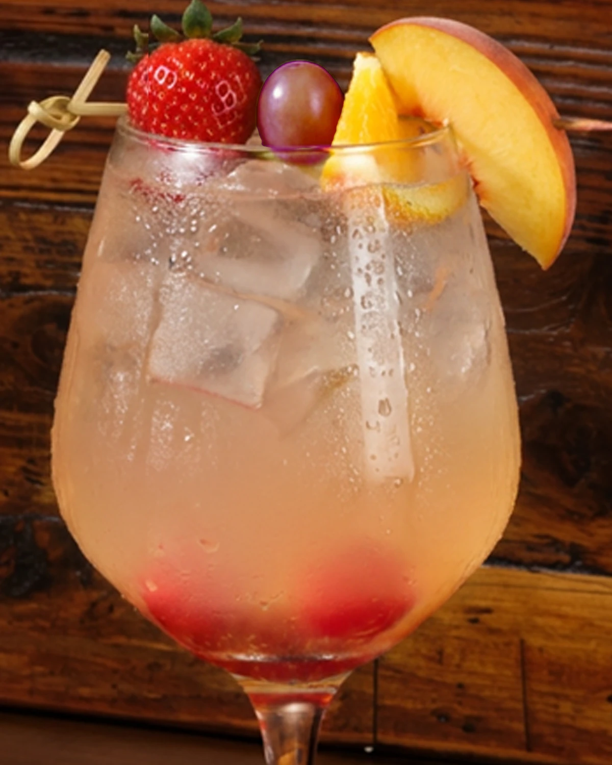 Just Peachy sangria in a stemmed glass over ice, garnished with a fresh peach slice, strawberry and grape