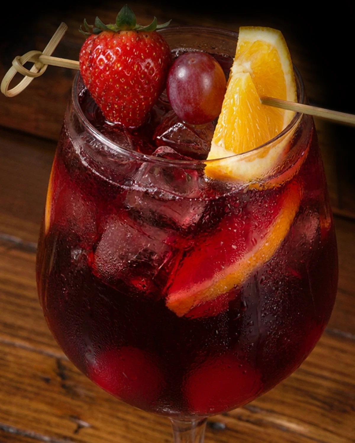 Traditional Red sangria in a stemmed glass over ice, garnished with strawberry, grape and fresh orange
