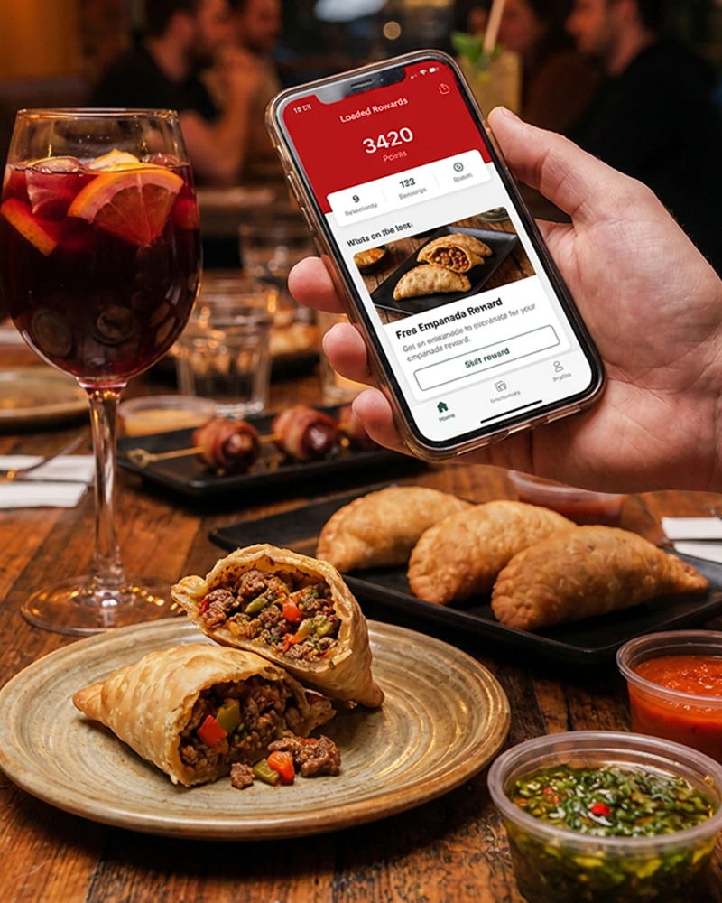 A guest holding up the Loaded Rewards app showing 3,420 points over a table of empanadas, chimichurri and sangria